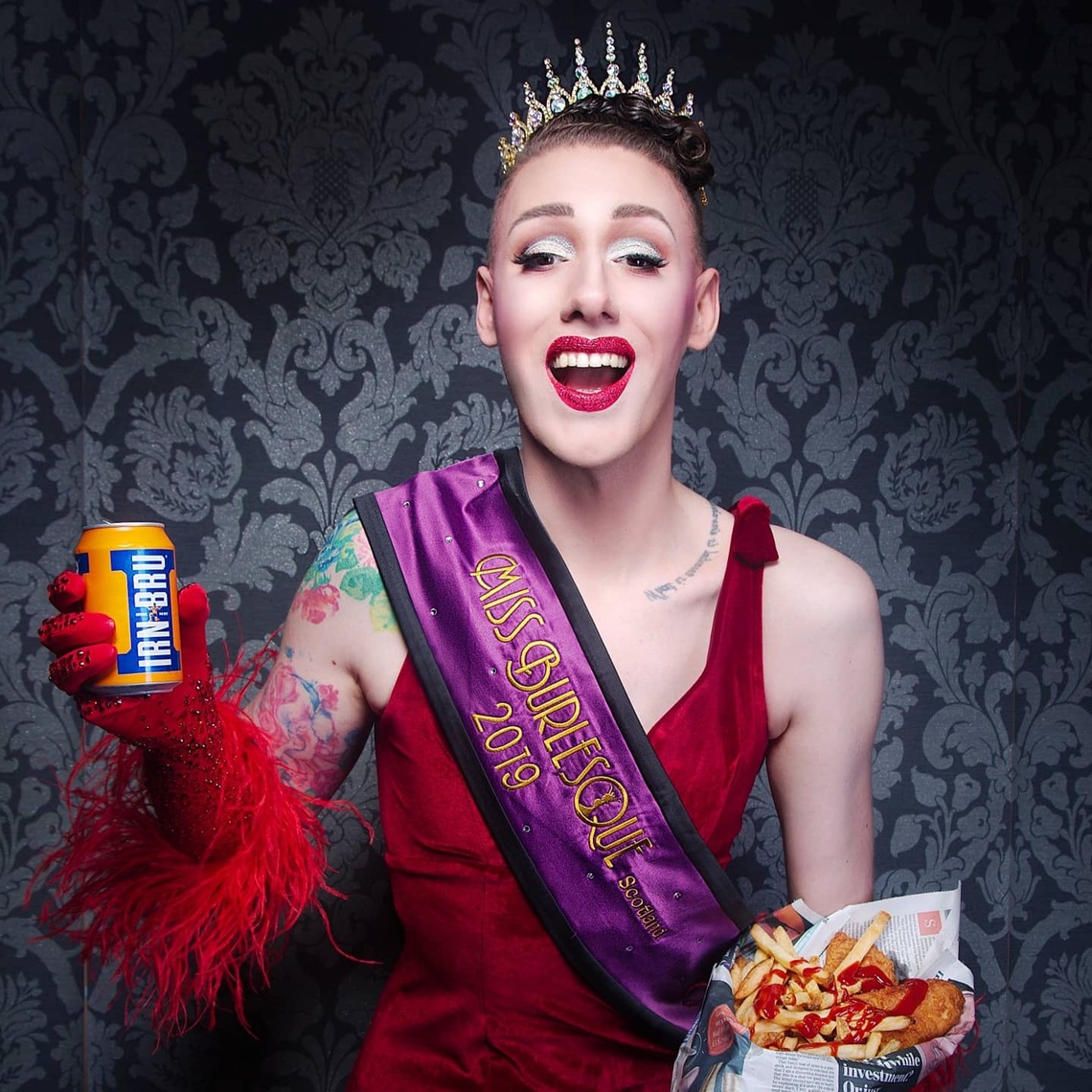 Tom Harlow performer wearing a crown red dress and purple sash
