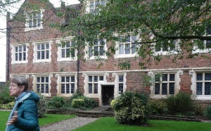 Someone standing in front of a large brick-built mansion with many windows