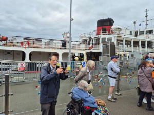 Superstructure of a small white ship morred next to a quay with people on it