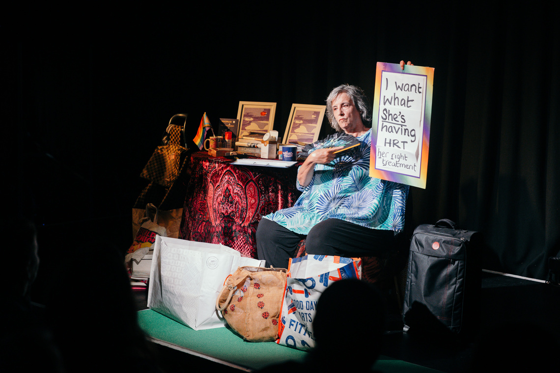 mature white woman sitting on stage surrounded by bags