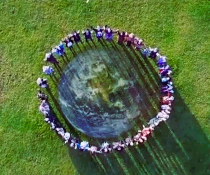 people stand in a circle, image of earth from space in the middle, overhead shot.