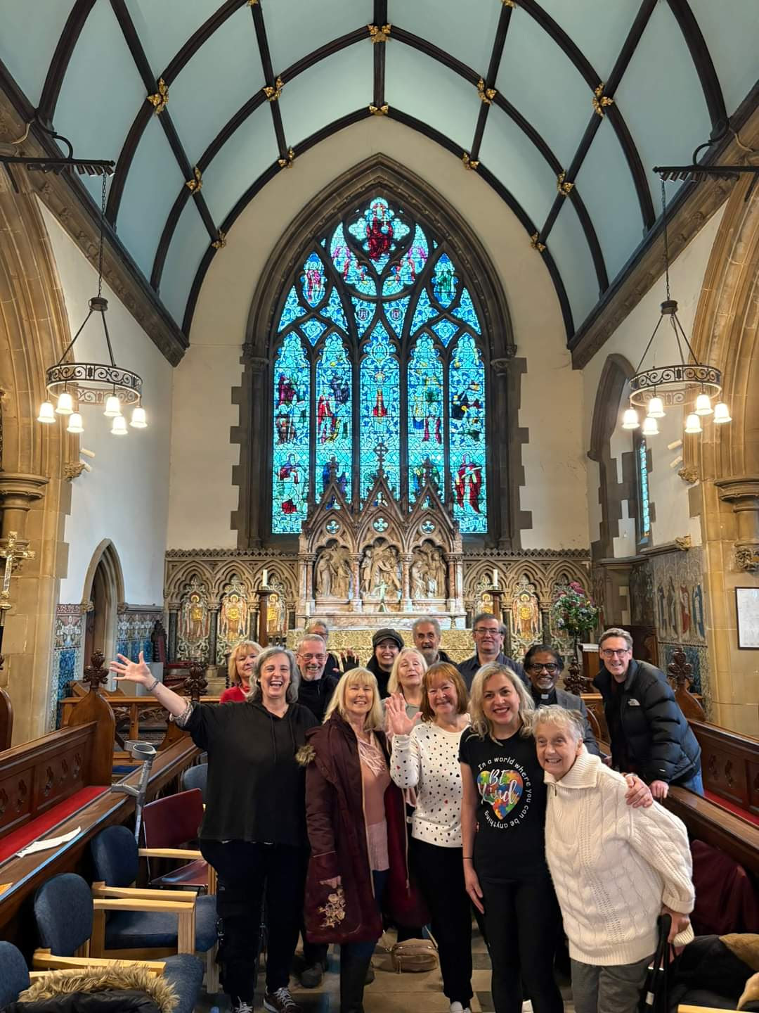 Agroup of singers in a beautiful Church space with wood pews and stained glass.