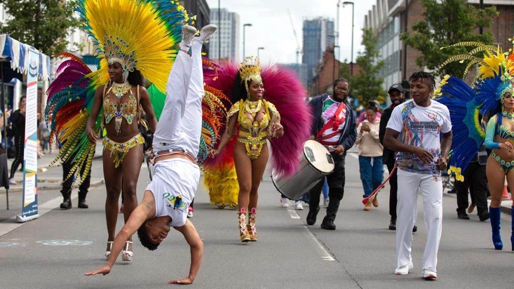 Photo of someone doing a handstand with women dressed in carnival costumes behind