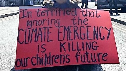 Photo of a protestor with a placard about he climate emergency killing our childrens future