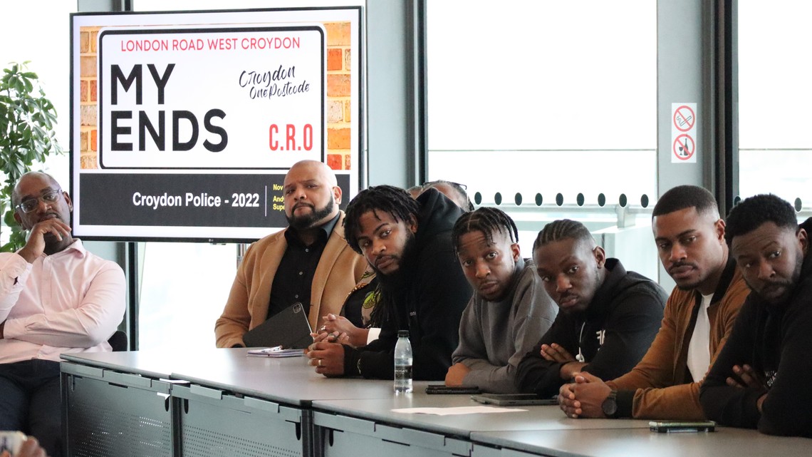 Photo of an event with the My Ends West Croydon sign and a row of young black men sitting at a table