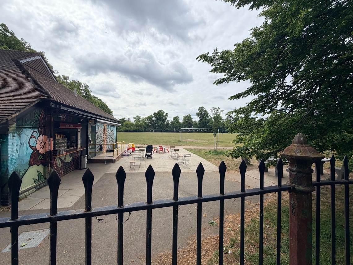 Medium close up of the cafe, with iron railings in the foreground and goal post in the distance on the grass beyond the cafe