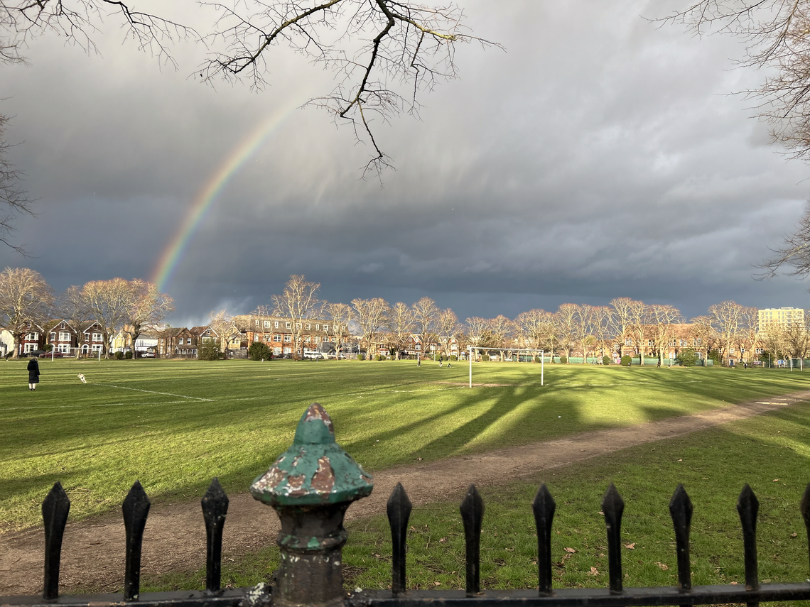 Top of wrought iron railings in the foreground looking across the open park where a rainbow arcs across the sky