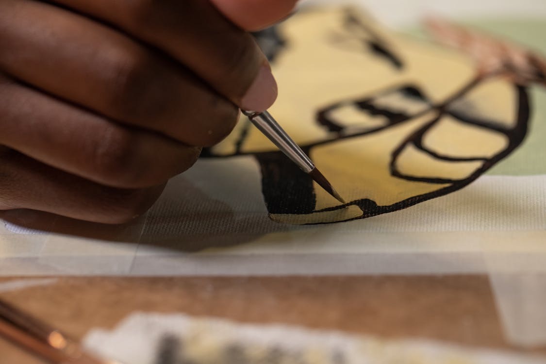 Close up of a hand holding a paintbrush. The artwork is shapes of green, red and yellow. Credit: artxadanna on Nappy.co