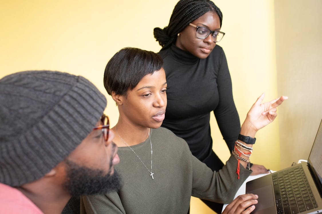 A black man and two black women looking at work together on a laptop. Credit: Nappy.co