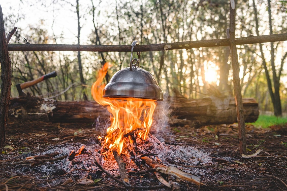 Metal cooking pot over an open fire with a woodland background
