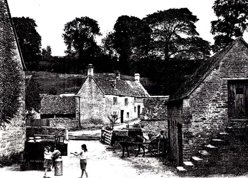Duntisbourne Leer - Leer Farm Yard with two girls playing next to a period motor vehicle loaded with milk churns with a further horse and cart being attended by a farmer