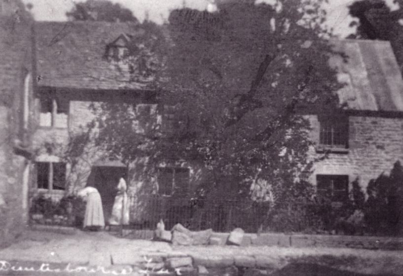 Duntisbourne Leer - view looking down towards the Dunt Stream and Holland's bakehouse and shop with two women working to the front of the shop