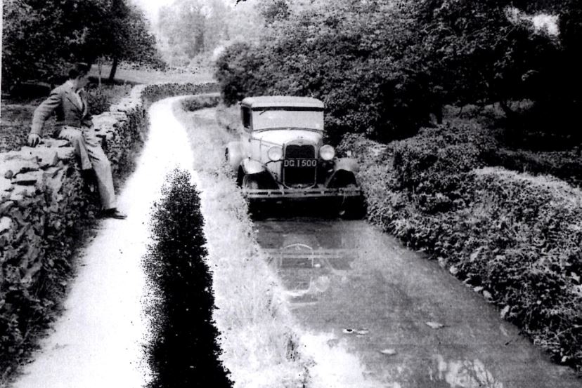 Long Ford - circa 1920s - showing period car driving through the ford whilst being watched from the side by a country Gentleman sat on a dry stone wall
