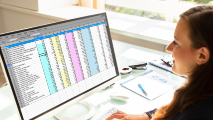 Woman smiles facing a computer that displays a table of data