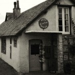 The building which for many years housed the post office was originally part of West Wembury farmstead, the rest of which stood immediately across the road. At one point the post office was on the upper floor, with the counter extending across the upstairs window and the teller standing with his back to it. Climbing the stairs was not popular with customers, especially the elderly. By the time this photo was taken in 1961 the owners (Dennis and Lena Baskerville) had moved it downstairs and put an associated shop in a former kitchen. The stamp machine just visible in the porch was another of their improvements. Today (2013) the building is occupied by a beauty salon - quite an indicator of change in the rural economy! &ndash; while the village post office and store are in an attached single-storey building to the right. 