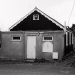 The Parish Room, also known as the Church Room, was paid for by the Cory family, owners of the Langdon Estate, in the 1900s. Although small, it provided a focus for meetings for those living in the eastern part of the parish. This role lasted for many decades, even though the first village hall was built soon after World War I, and was itself replaced by the War Memorial Hall in the early 1950s. Originally the parish room had no water supply, but more than half a century after it was built this was corrected and a kitchen and toilets were added. In this photo, the light-coloured front of the hall is a small extension in which the toilets were housed. Eventually declared unsafe, the Parish Room was demolished in 2013. 