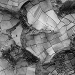 Langdon Court is clearly visible as a white square in the south west. Its landscape garden lies immediately east, leading down to woodland in the valley. 1930s Wembury dominates the south east. The right angle visible on the road passing through the buildings is the sharp bend at the top of Church Road. Most of the buildings here are houses built on land sold off after the break-up of the Langdon Estate in 1927 - typical inter-war ribbon development.