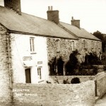 These nineteenth-century employees&rsquo; cottages in Traine Road (near the Odd Wheel pub) were built on a former orchard for Mr Ralph Dawson of Wembury House.  The 1881 census shows that, in contrast to the nearby cottages on Knighton Hill, the families living here were not agricultural. For example, one family head was a groom, another a carrier and a third a Chelsea Pensioner. In the early 20th century the nearest cottage was run for many years as the Knighton Post Office by Miss Minnie Perring, later Mrs Brown. The business was based in the living room, which also contained the black-lead range for cooking. The back room contained the kitchen plus a walk-in larder and doubled as a dining room. The front bedroom upstairs was made into a parlour, while Mr and Mrs Brown slept in the back bedroom. The children, meanwhile, used a wooden hut in the corner of the Browns&rsquo; field in front of the cottages.  This hut was painted maroon and was still there in the 1950s &ndash; but was now a chicken house. 