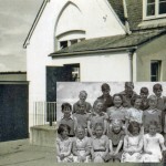 The final building in West Wembury was the original school. Although it played such an important role in the community, there are very few photographs of the building. Built of granite, by the time this picture was taken in the 1950s it had been rendered. The glimpse of Traine Down to the left of the picture hints at the school's attractive location. The inset photograph is a school photo from the early 1950s. The children would have rushed through the door behind to play in this yard.